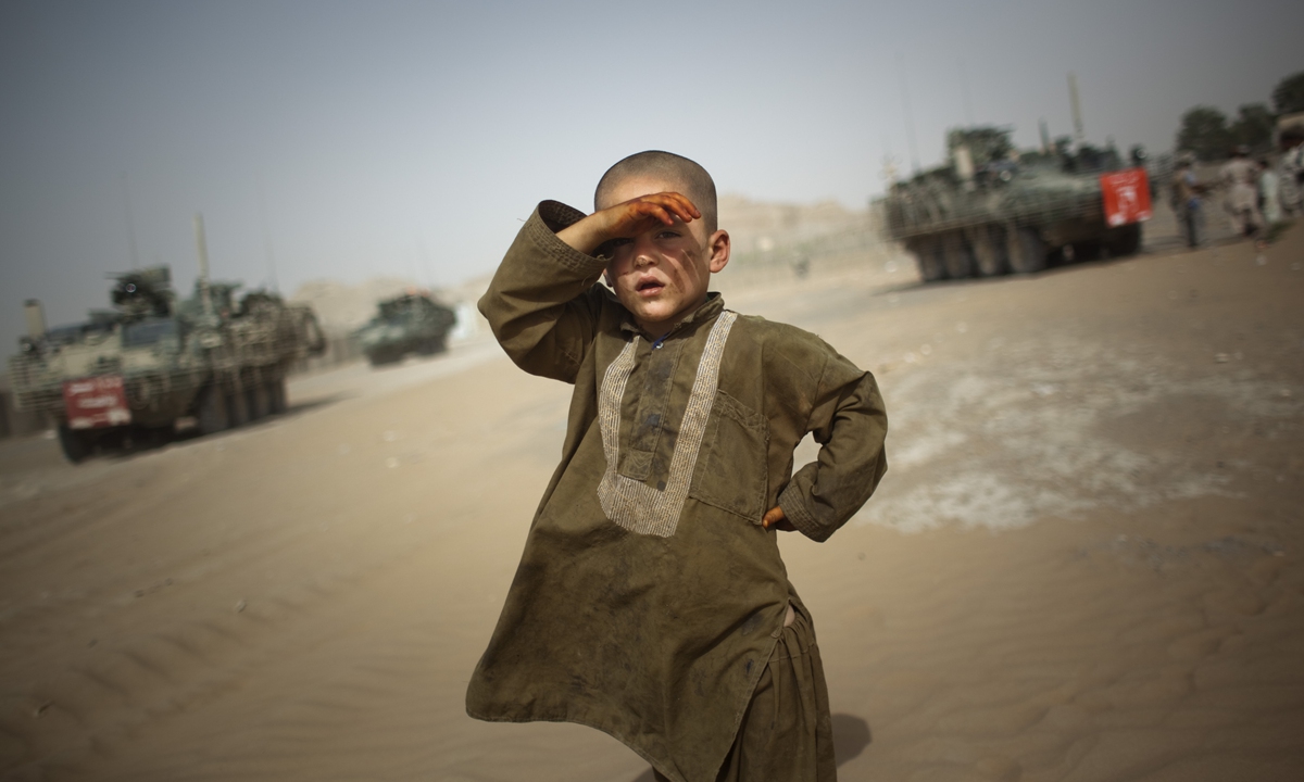A child looks on as military vehicles of US Army's 5th Stryker Brigade drive past his village near Kandahar, Afghanistan, on August 6, 2009. Photo: VCG