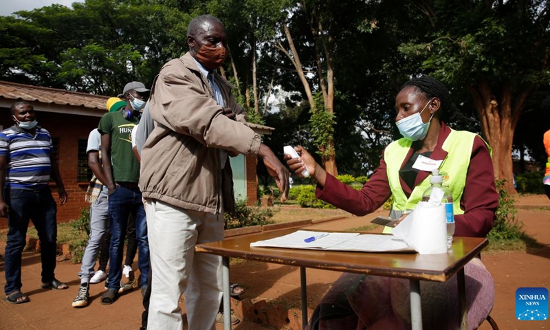 A staff member checks body temperature of a voter at a polling station in Harare, Zimbabwe, on March 26, 2022.Photo:Xinhua