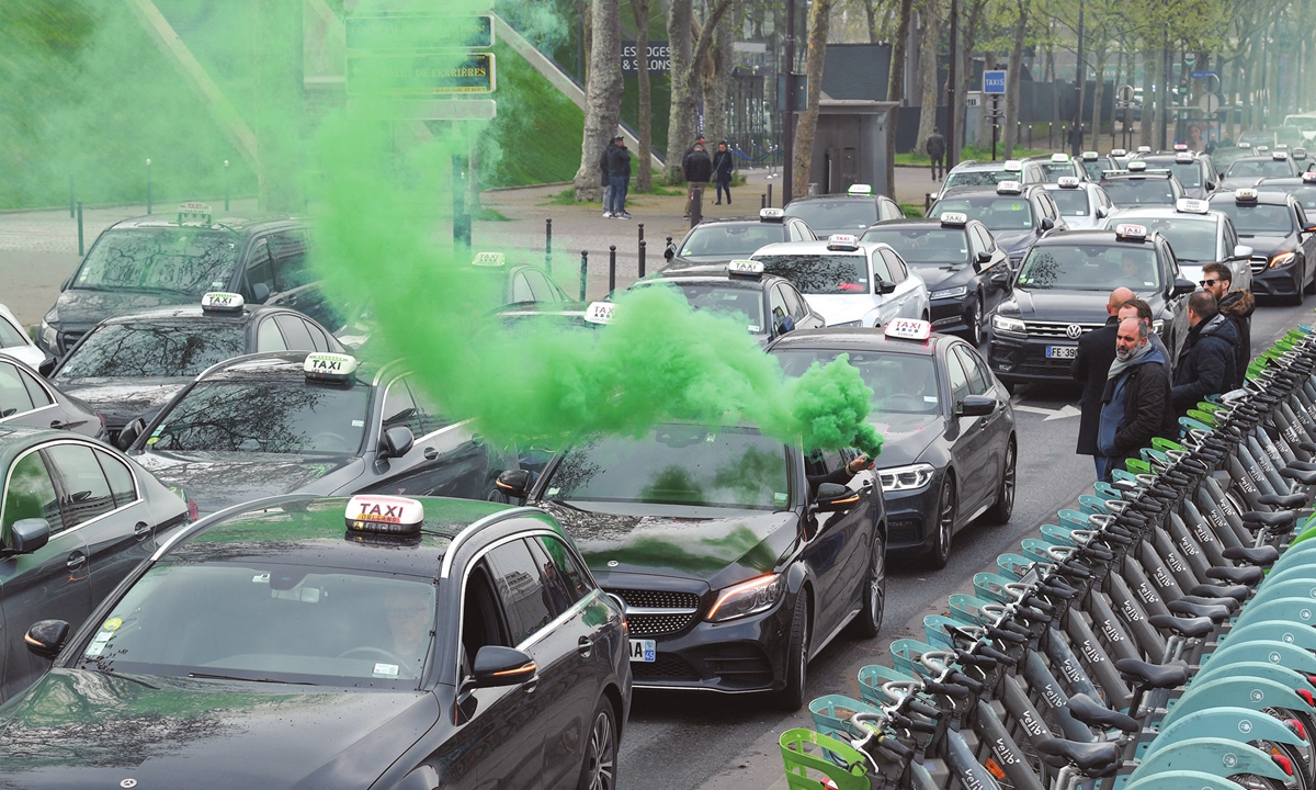 Holding a green flare out the car window, dozens of taxis protest against a hike in fuel prices as they drive from Roissy-Charles de Gaulle international airport to Bercy, Paris on March 30, 2022. The Ukraine crisis and the Western sanctions against Russia have caused a fuel price surge in Europe. Photo: AFP