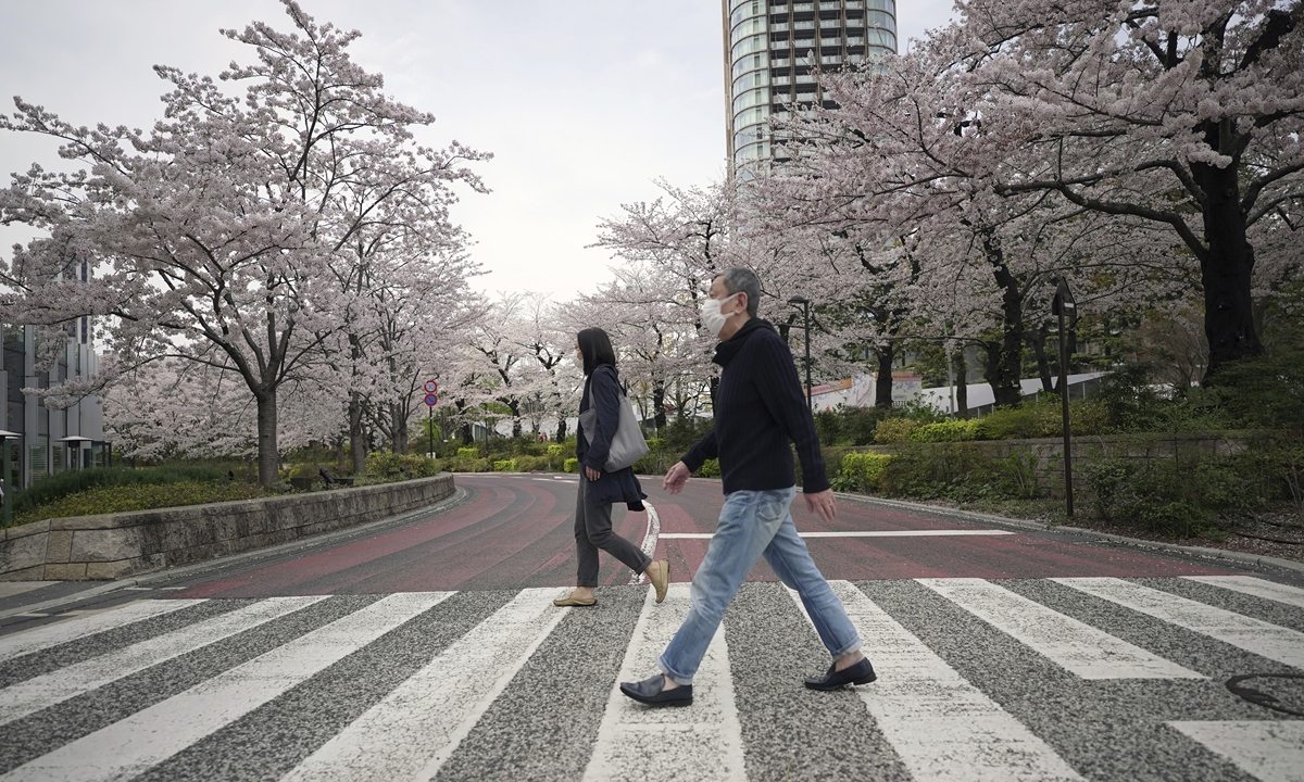 People walk along a pedestrian crossing surrounded by blooming cherry blossoms in Tokyo on March 31, 2022. Cherry blossoms, or