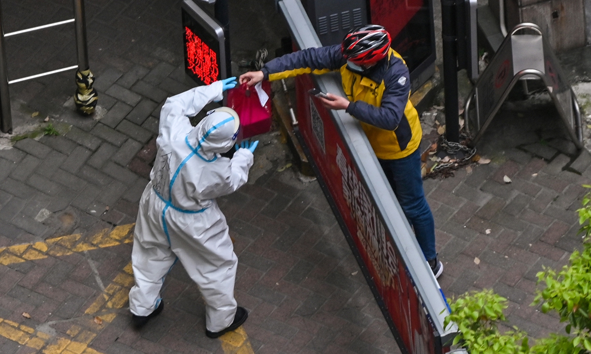 A community worker wearing protective suit receives an item from a deliveryperson at the entrance of a sealed compound in Jing' an district in Shanghai on April 5, 2022. Photo: AFP