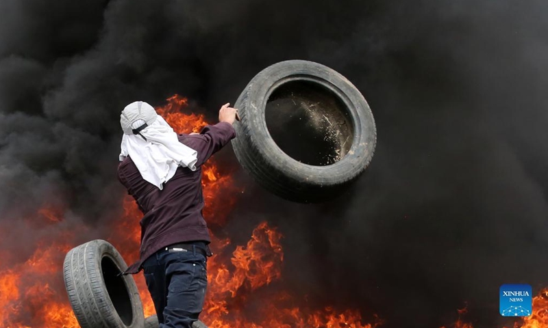 A Palestinian protester burns tires during clashes with Israeli soldiers after a protest against the expanding of Jewish settlements in Kufr Qadoom village near the West Bank city of Nablus, on April 8, 2022.(Photo: Xinhua)
