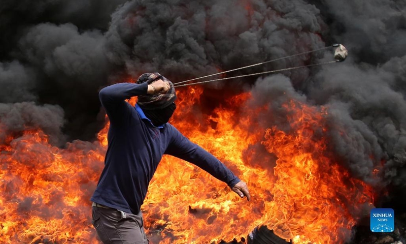 A Palestinian protester uses a slingshot to hurl a stone at Israeli soldiers during clashes after a protest against the expanding of Jewish settlements in Kufr Qadoom village near the West Bank city of Nablus, on April 8, 2022.(Photo: Xinhua)