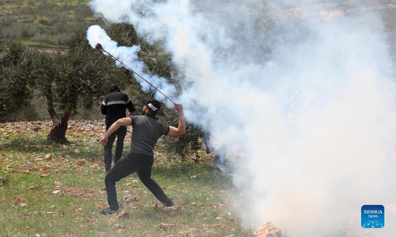 A Palestinian protester uses a slingshot to throw back a tear gas canister fired by Israeli soldiers during clashes after a protest against the expanding of Jewish settlements in the village of Beita, south of the West Bank city of Nablus, April 8, 2022.(Photo: Xinhua)