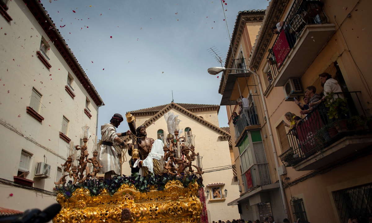 People throw flower petals as a float depicting Jesus Christ bearing the cross passes by during a Holy Week procession in Granada, Spain, on April 11, 2022.  Photo: AFP