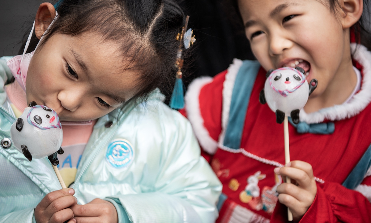 From left: An artist works on a sugar Bing Dwen Dwen figurine. Two children enjoy their sugar Bing Dwen Dwen figurines. Photos: IC