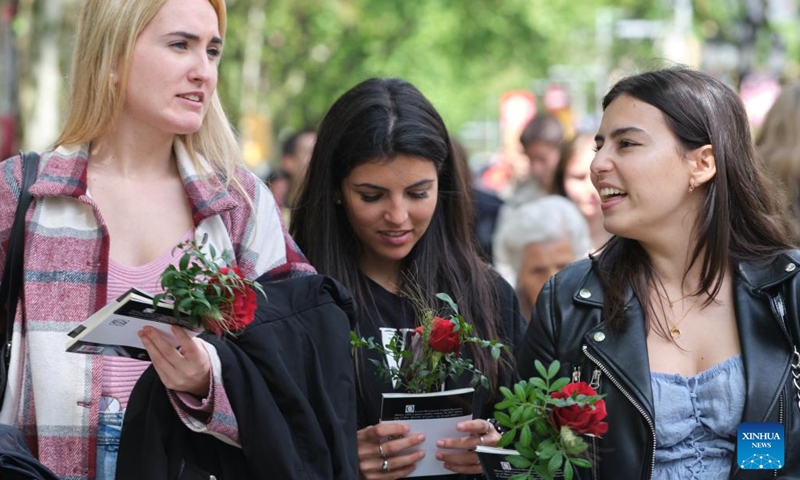 People holding roses walk on the street in Barcelona, Spain, April 23, 2022. St. George's Day usually sees the streets of Barcelona filled with parades of people exchanging books and flowers with their loved ones. (Xinhua/Meng Dingbo)