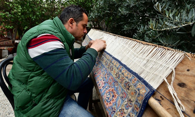 Omar Rawas, a carpet weaver, is seen fixing carpets at his workshop in Syria's northern city of Aleppo on March 8, 2022.(Photo: Xinhua)