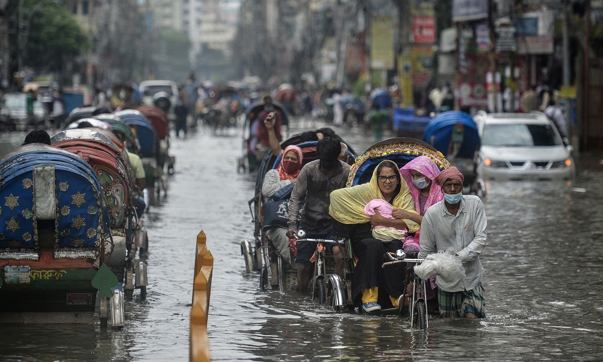 Cycle rickshaw drivers wade through a waterlogged street carrying their passengers after a heavy downpour in Dhaka, Bangladesh on July 4, 2021. Photo: AFP