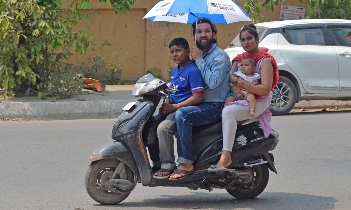 A motorist (center) holds an umbrella while driving a scooter with his family along a road on a hot summer day in Amritsar, India on May 1, 2022. Photo: AFP