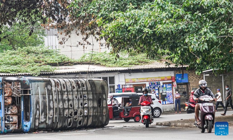 People pass a bus destroyed in the clashes few days ago during a few hours' relaxation of the ongoing curfew in Colombo, Sri Lanka, May 12, 2022. Sri Lanka imposed a nationwide curfew following violent clashes in the capital Colombo on May 9.(Photo: Xinhua)