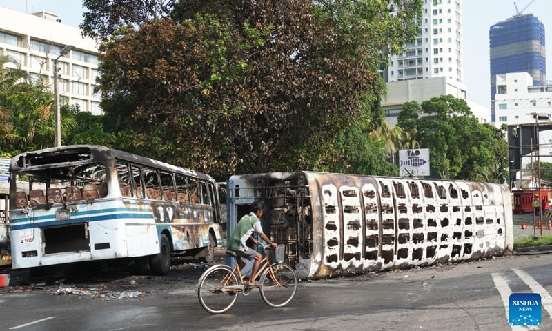 A man rides past buses destroyed in the clashes few days ago during a few hours' relaxation of the ongoing curfew in Colombo, Sri Lanka, May 12, 2022. Sri Lanka imposed a nationwide curfew following violent clashes in the capital Colombo on May 9.(Photo: Xinhua)