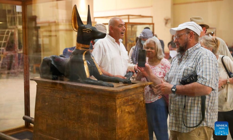 Tourists view the statue of god Anubis discovered at the tomb of king Tutankhamun, at the Egyptian Museum in Cairo, Egypt, on May 14, 2022. As a funerary deity, Anubis is associated with mummification, funerary rituals, and the cemetery in ancient Egyptian myth, usually depicted as a black canine, or a man with canine head. It can be found at large numbers of pharaonic antiquities at the world-known Egyptian Museum. (Xinhua/Sui Xiankai)