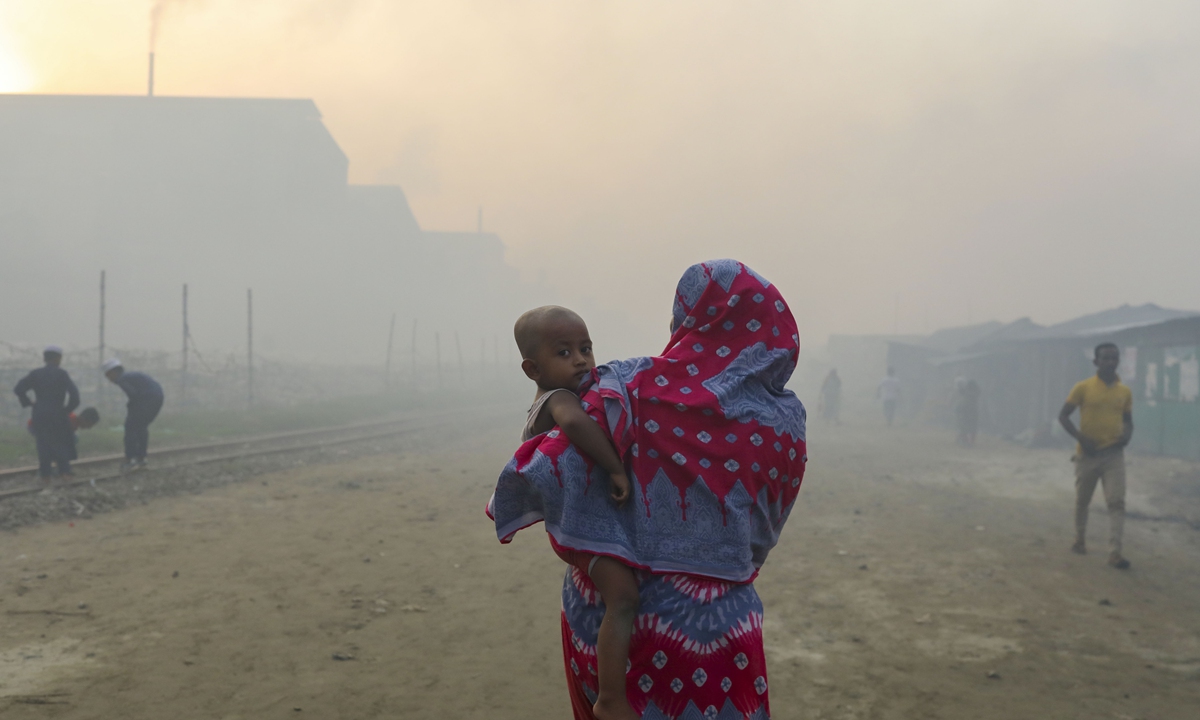 A woman is seen holding her child walking in an air-polluted area as smoke rises from a re-rolling mill in Dhaka, Bangladesh, on May 16, 2022. Based on a recent study published in Science Advances in April 2022, air pollution responsible for 24,000 premature deaths in Dhaka from 2005 to 2018, according to local news.Photo: VCG