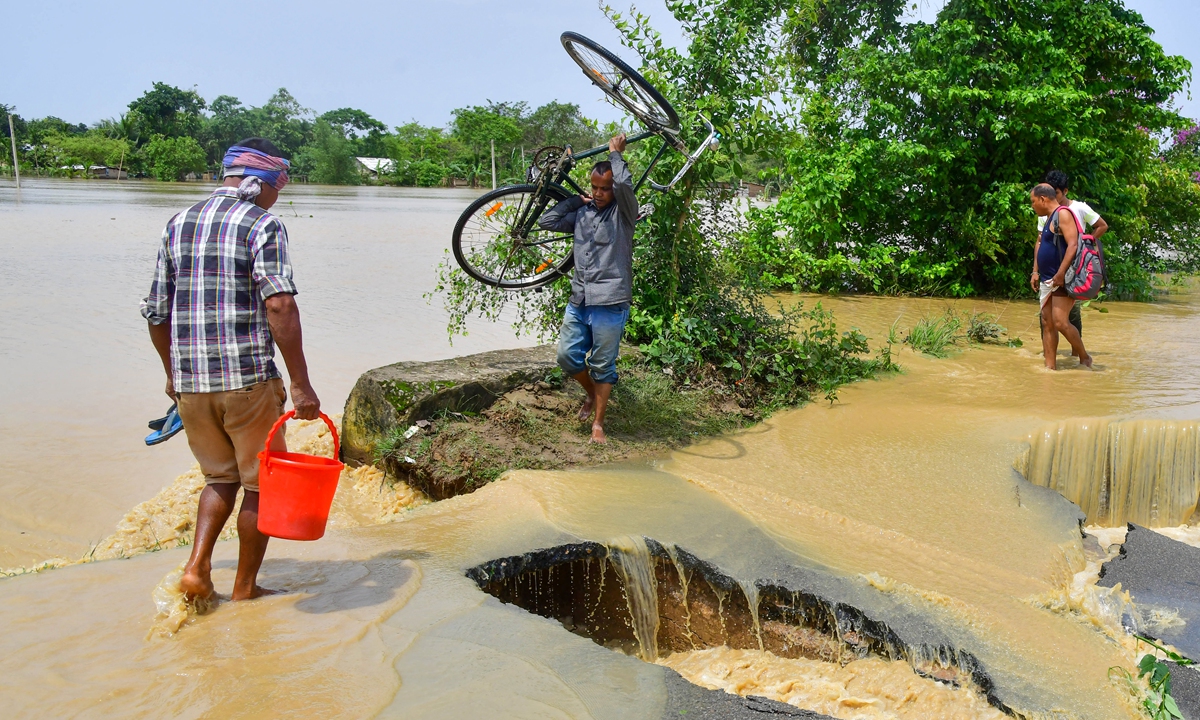 A man carrying his bicycle crosses a damaged road due to flooding after heavy rains in Nagaon, India on May 19, 2022. At least 10 people died in floods and landslides this week due to heavy rains in the country. Photo: AFP