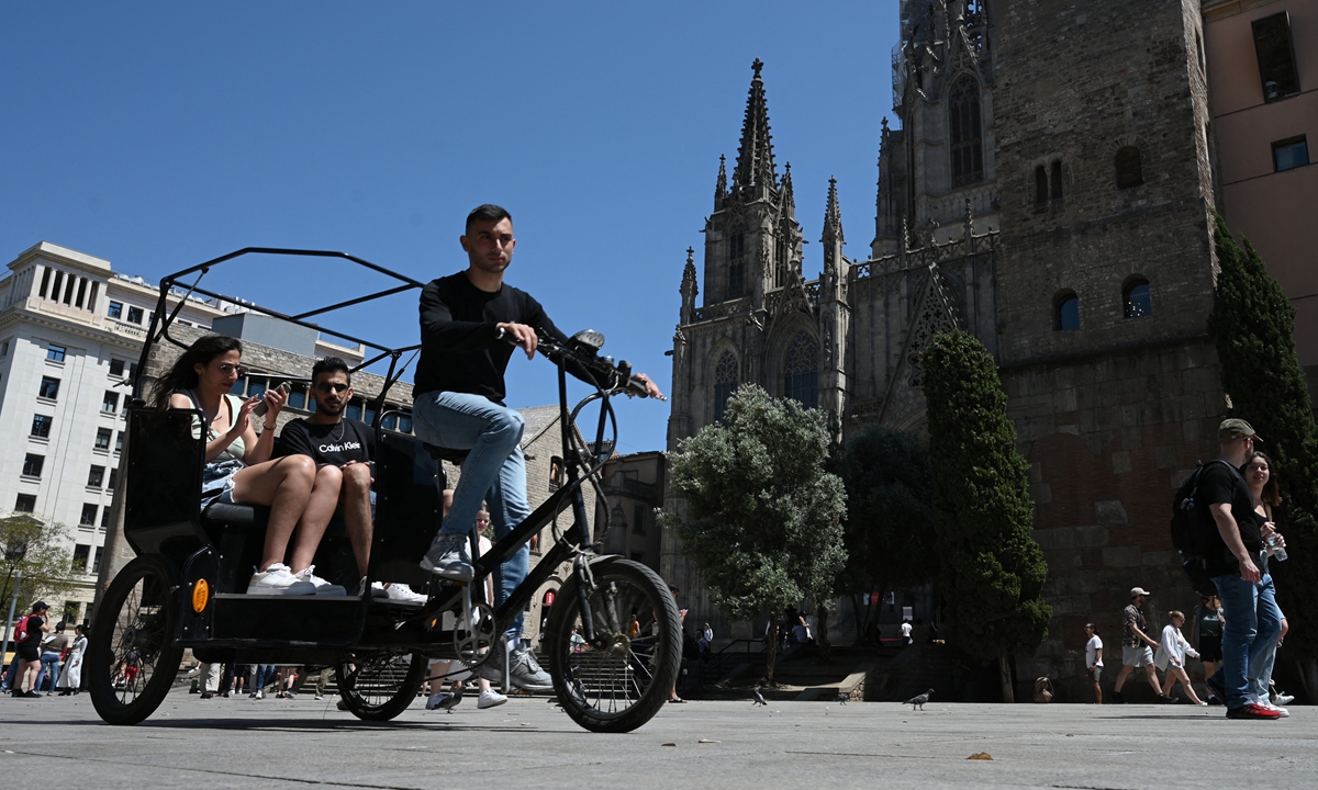 Tourists enjoy a ride on a bike taxi at Plaza de la Catedral in Barcelona, on May 11, 2022. Photo: AFP
