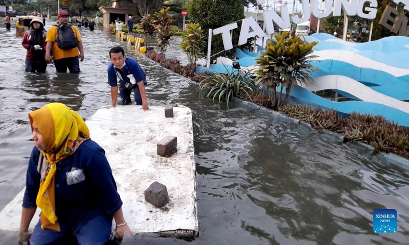 Photo taken with a mobile phone on May 23, 2022 shows people walking in flood water triggered by high tides and broken embankment at Tanjung Emas Port on the coast of Semarang, Central Java, Indonesia.(Photo: Xinhua)