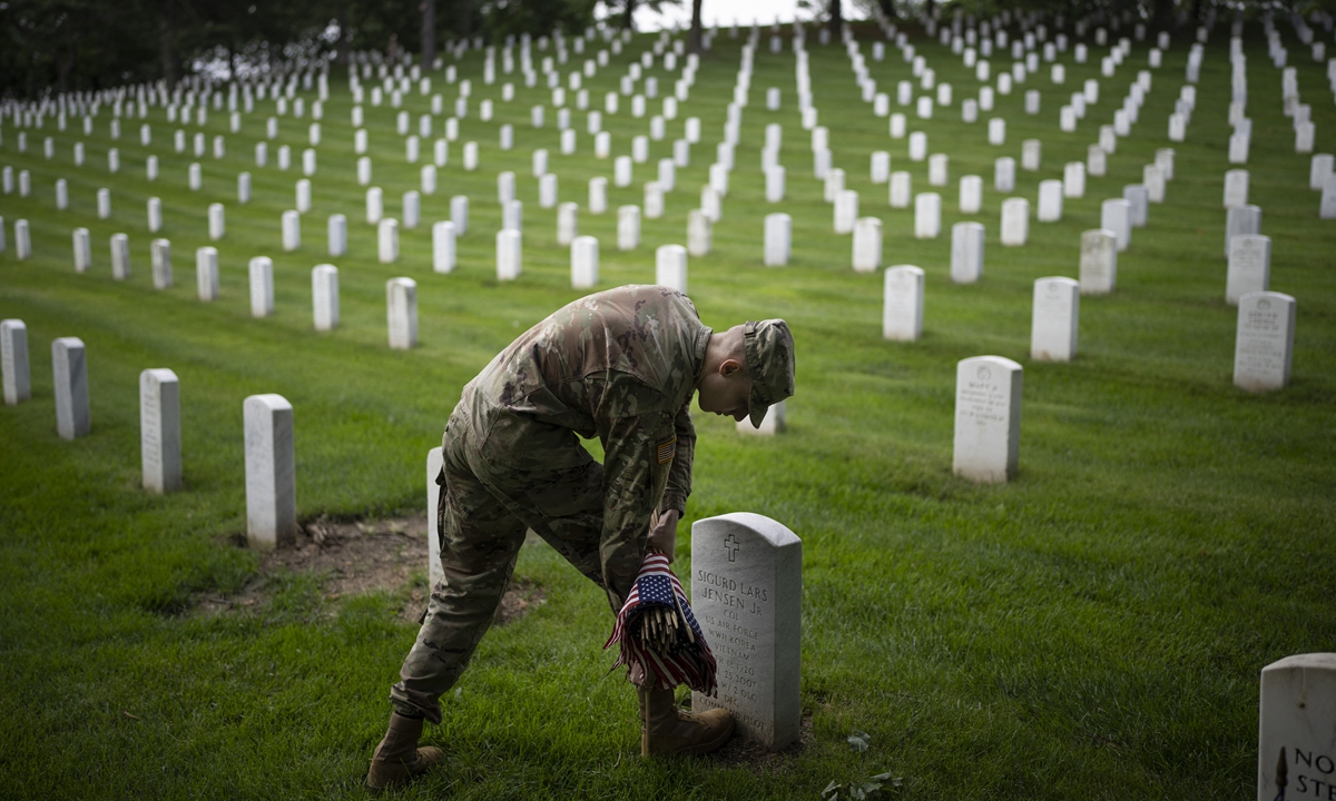 A member of the 3rd US Infantry Regiment places flags at the headstones of US military personnel buried at Arlington National Cemetery, in preparation for Memorial Day, on May 26, 2022 in Arlington, Virginia. Photo: AFP