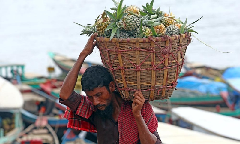A man carries a basket of pineapples at a floating market in Rangamati, Bangladesh, on May 22, 2022.(Photo: Xinhua)