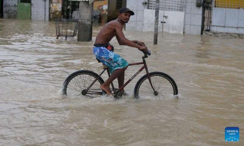 A man rides a bike on a flooded street after heavy rains in Recife, Brazil, June 3, 2022. The death toll from heavy rains in Recife, capital of the Brazilian state of Pernambuco, and its metropolitan area has risen to 128, local authorities said Friday. (Photo by Lucio Tavora/Xinhua)