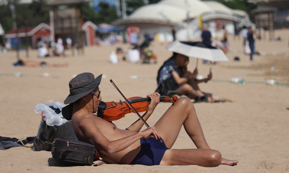 A tourist plays a violin at a beach in Qingdao, East China's Shandong Province, May 27, 2022. China's National Meteorological Center issued a yellow alert on May 27: most parts of Northern China, including Qingdao, are expected to see high temperatures above 35 C during the day on May 28.Photo:IC