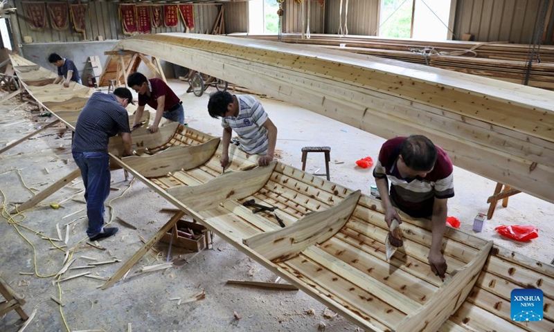 Craftsmen fill waterproofing material in a new dragon boat at Fangzhongxiong dragon boat factory in Fangzhuang Village of Nantong Township in Minhou County of Fuzhou, southeast China's Fujian Province, May 30, 2022. Fangzhuang, known as Dragon Boat Village, has a traditional dragon boat manufacturing history for more than 700 years. Every year, more than 200 hand-made wooden boats, carefully built by craftsmen, are sold nationwide and even overseas from the village.(Photo: Xinhua)