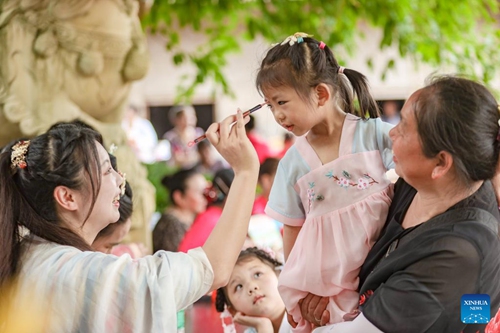 A local volunteer marks a girl on her forehead with a brush dipped in realgar to ward off evil spirits as a traditional custom during the Dragon Boat Festival at Guangjing Village of Renhe Township in Shehong City, southwest China's Sichuan Province, June 2, 2022. The Dragon Boat Festival will fall on June 3 this year. (Photo by Liu Changsong/Xinhua)