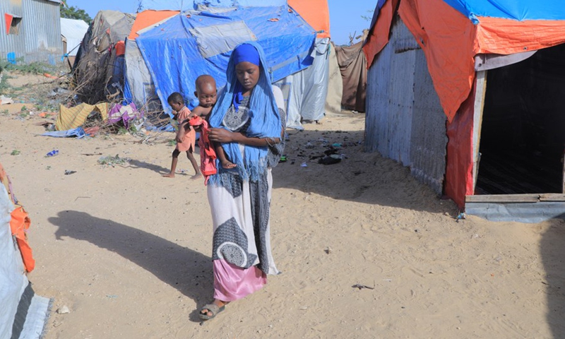 A woman carrying a child is seen at a camp on the outskirts of Mogadishu, capital of Somalia, Jan. 13, 2022. (Photo: Xinhua)