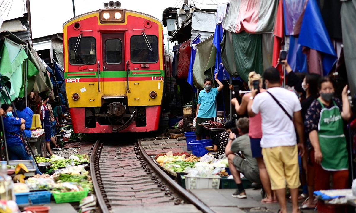 Vendors and visitors stand next to a passenger train passing through the Mae Klong Railway Market in Samut Songkhram province, around 80 kilometers southwest of Bangkok, on June 4, 2022. Photo: AFP