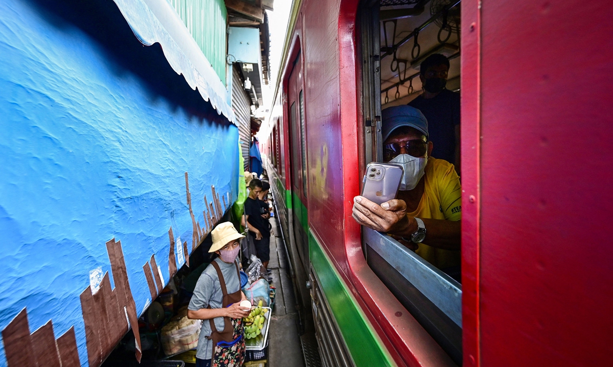 A passenger is making a video with his mobile phone while passing through the Mae Klong Railway Market on, June 4, 2022.  Photo: AFP