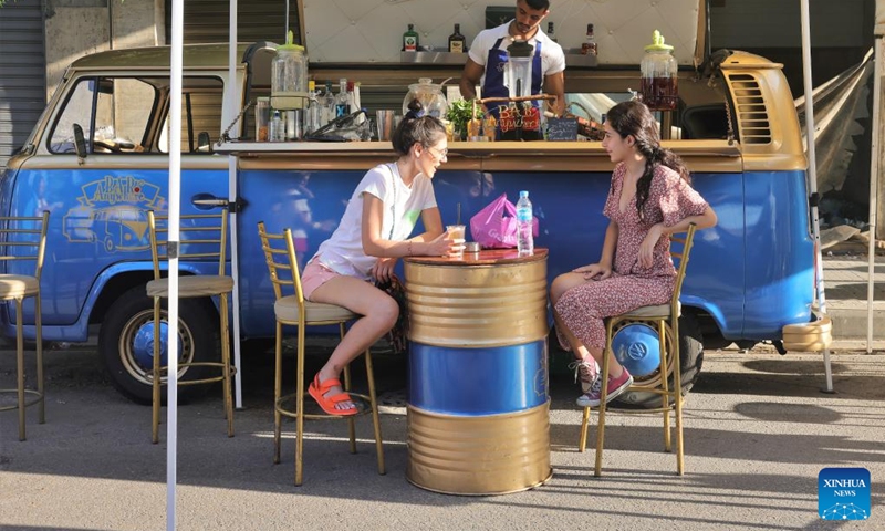 Two young women drink and chat at a food booth during a street festival held in Mar Mikhael, in Beirut, Lebanon, June 19, 2022. (Photo: Xinhua)