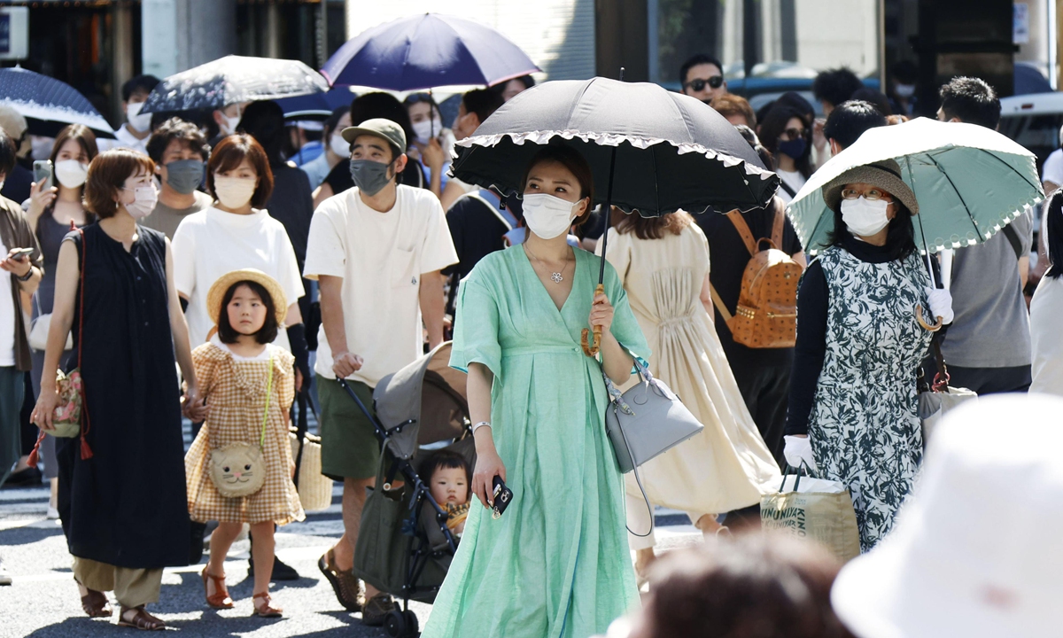 People wearing face masks for protection against coronavirus walk under the glaring sun in Tokyo's Ginza shopping area, Japan on June 25, 2022. The city of Isesaki in Gunma Prefecture registered 40.2 C the same day, a national record high temperature for June, the Japan Meteorological Agency said. Photo: AFP
