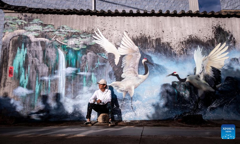 Liu Zhicheng takes a break with his wall painting in the background in Yongsheng County, Lijiang City, southwest China's Yunnan Province, June 24, 2022.Photo:Xinhua
