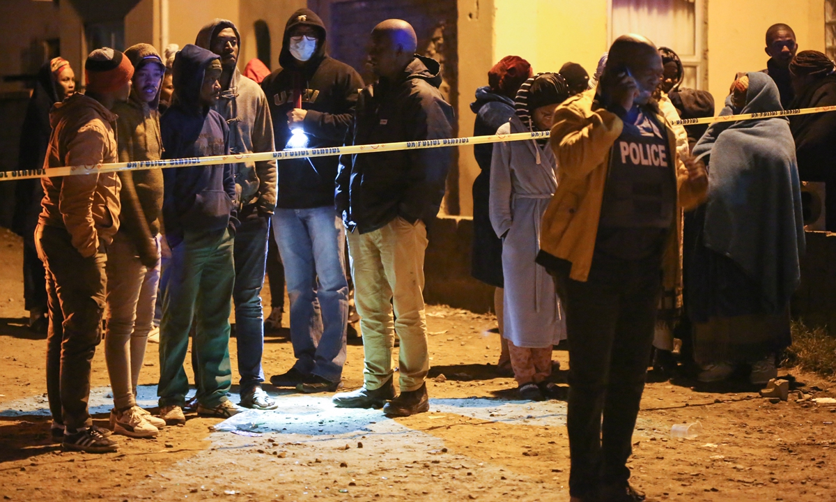 Members of the community and family wait for news outside a township pub as a police officer talks on a phone in South Africa's southern city of East London on June 26, 2022, after 21 teenagers died. Photo: AFP