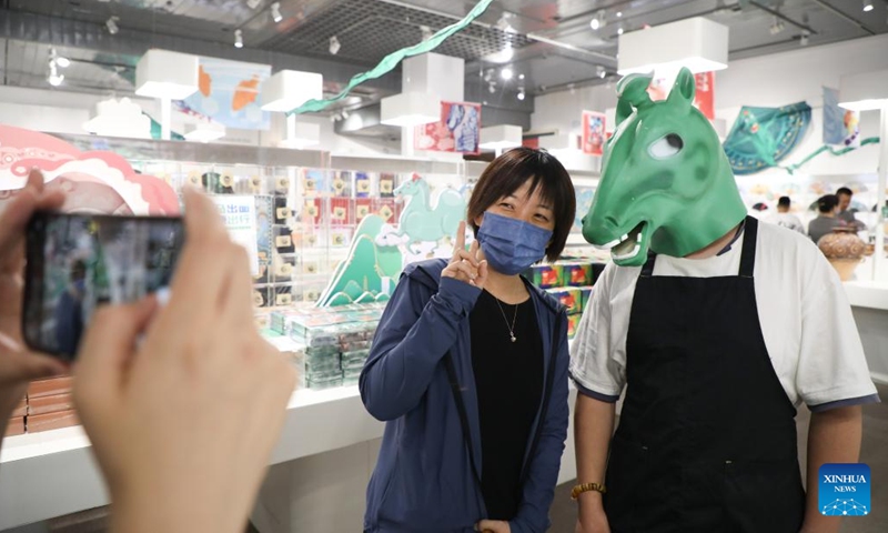 A tourist (L) poses for photos with a staff member wearing a headgear depicting an ancient bronze horse statue at a store in the Gansu Provincial Museum in Lanzhou, capital of northwest China's Gansu Province. China), June 28, 2022. The bronze horse statue, popularly known as A Bronze Galloping Horse Stepping on a Flying Swallow, was unearthed in the 1960s from the Han Dynasty Leitai Tomb of the East (25-220 AD) in Wuwei and is now housed in the Gansu Provincial Museum.  (Photo: Xinhua)