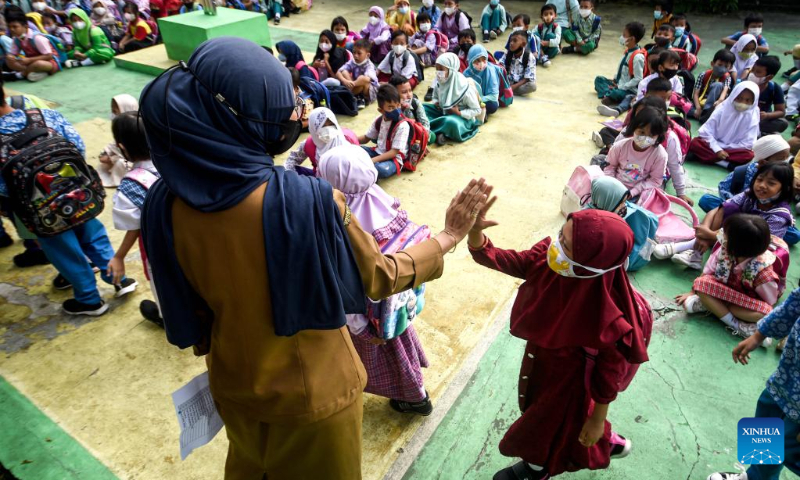 A student greets her teacher after the first-day orientation of school year 2022-2023 at Jombang elementary school in South Tangerang of Banten Province, Indonesia, July 11, 2022. (Xinhua/Agung Kuncahya B.)