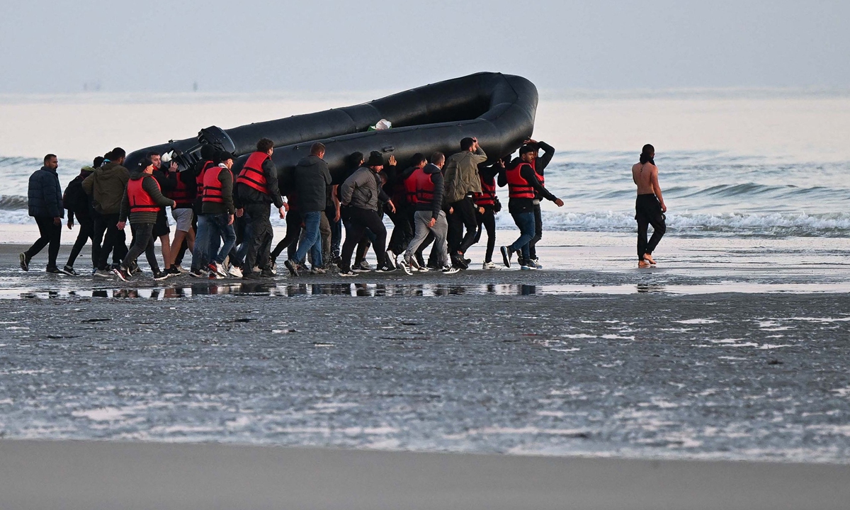 About 40 migrants, from various origins, carry an inflatable boat toward the water before they attempt to cross the Channel illegally to Britain, near the northern French city of Gravelines on July 11, 2022. Photo: VCG