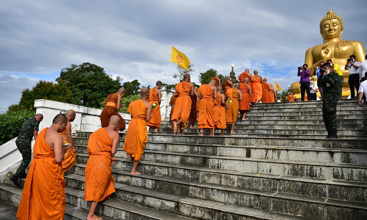 Buddhist monks holding flowers walk toward a giant Buddha statue as they perform religious rites to mark Asahna Bucha Day in Thailand's southern Narathiwat Province on July 13, 2022. Photo: VCG