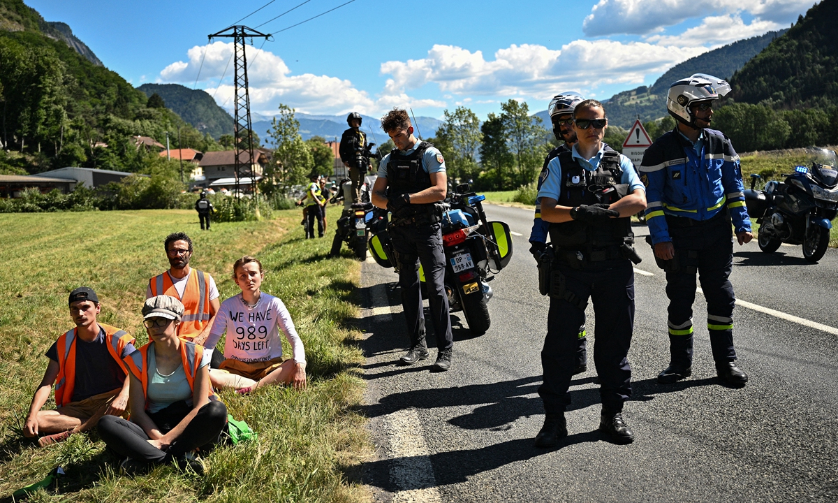 French gendarmes (right) stand by environmental protesters after their protest action temporarily immobilized the pack of riders during the 10th stage of the 109th edition of the Tour de France cycling race in the French Alps on July 12, 2022. Photo: AFP