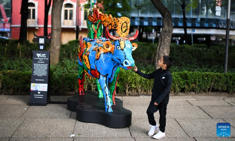 A kid touches a cow sculpture displayed during the CowParade event in Mexico City, Mexico, July 24, 2022. (Xinhua/Xin Yuewei)