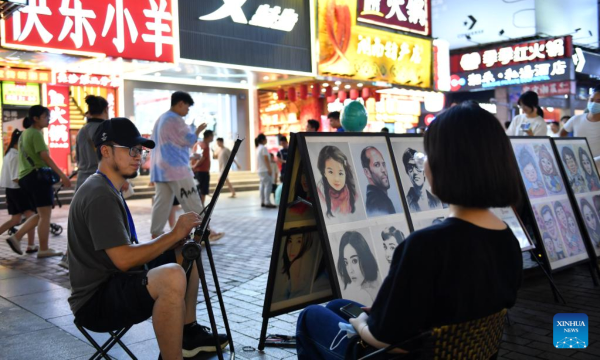 A painter (L, front) draws a portrait for a tourist at Huangxing Road in Changsha, central China's Hunan Province, July 29, 2022. With stimulus measures taken by local authorities, Changsha has seen a robust recovery of the nighttime economy. Photo:Xinhua