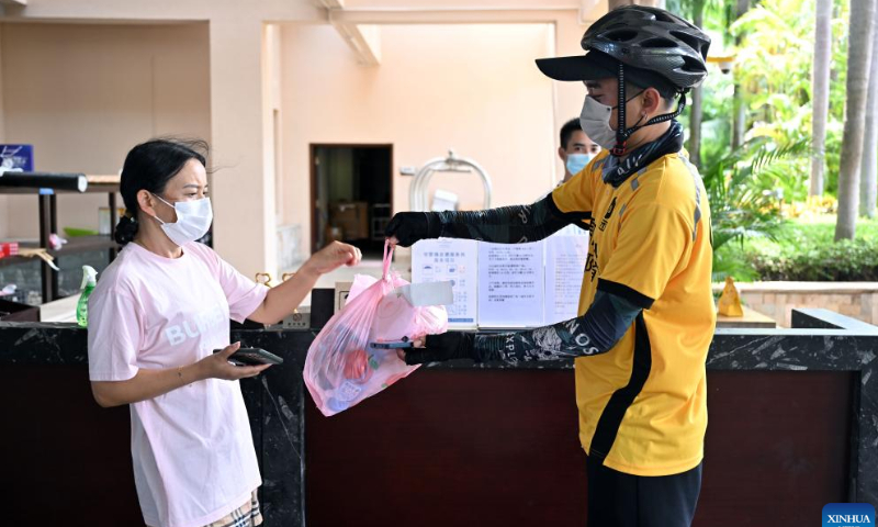 A tourist receives goods she ordered online from a delivery man outside a hotel in Sanya, south China's Hainan Province, Aug. 7, 2022. Prevention and control measures have been taken in Sanya to fight against the new resurgence of COVID-19 in the city.  Photo: Xinhua