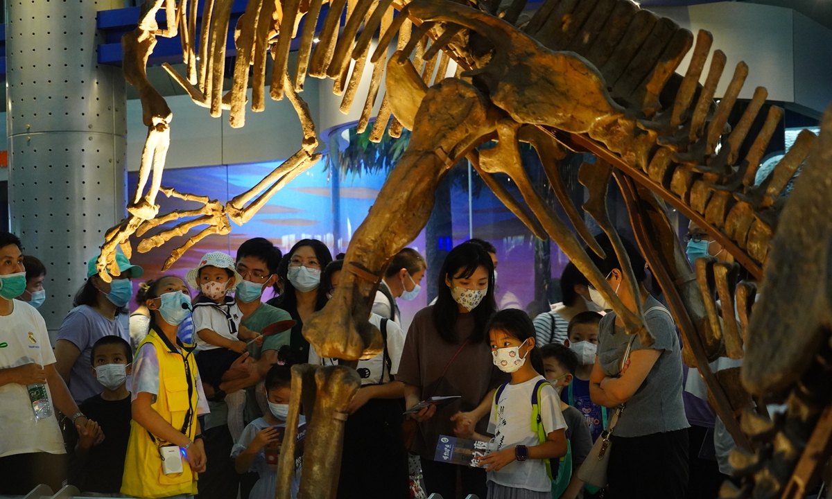 Children and parents listen to a presentation in front of a dinosaur skeleton at the Beijing Museum of Natural History on August 3, 2022. The museum is open to 800 visitors at night from August 2-6, with bookings required. Visitors can have their museum passport stamped for each question that's answered about animals and nature. Photo: VCG
