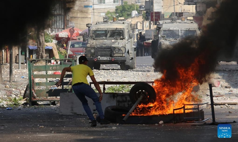 A Palestinian protester hurls stones at Israeli military vehicles during clashes in the West Bank city of Nablus on Aug. 9, 2022. Three Palestinians were killed and 40 others were injured early Tuesday in clashes with the Israeli soldiers in the northern West Bank city of Nablus, Palestinian medics and eyewitnesses said.(Photo: Xinhua)