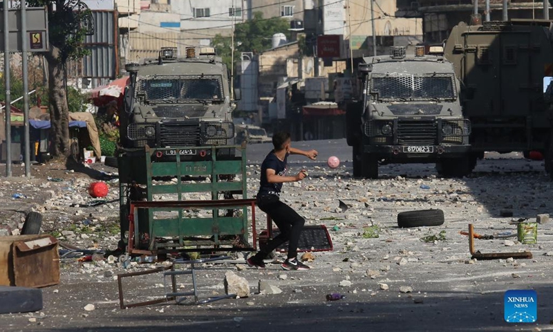 A Palestinian protester hurls stones at Israeli military vehicles during clashes in the West Bank city of Nablus on Aug. 9, 2022. Three Palestinians were killed and 40 others were injured early Tuesday in clashes with the Israeli soldiers in the northern West Bank city of Nablus, Palestinian medics and eyewitnesses said.(Photo: Xinhua)