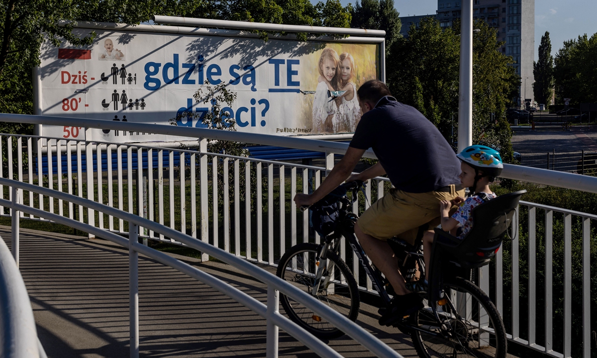A cyclist with a child in his backseat crosses a bridge near a billboard with the lettering reading 'Where are these children?' in Warsaw, Poland, on August 5, 2022. Photo: AFP