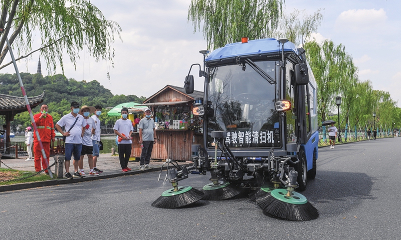 Travelers stop to watch a smart driverless cleaning machine at work along the West Lake in Hangzhou, East China's Zhejiang Province on August 10, 2022. The smart cleaning gear, powered by 5G connectivity, autonomous driving and visual recognition, among other technologies, was recently put into use in the famed scenic site. Photo: cnsphoto
