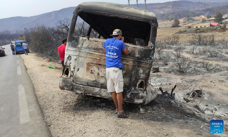 People check a vehicle damaged in a forest fire in El Tarf province, Algeria, on Aug. 18, 2022. At least 37 people were killed and 235 others injured in forest fires that have ravaged large parts of the country, said a statement of the Algerian civil protection authority on Thursday.(Photo: Xinhua)