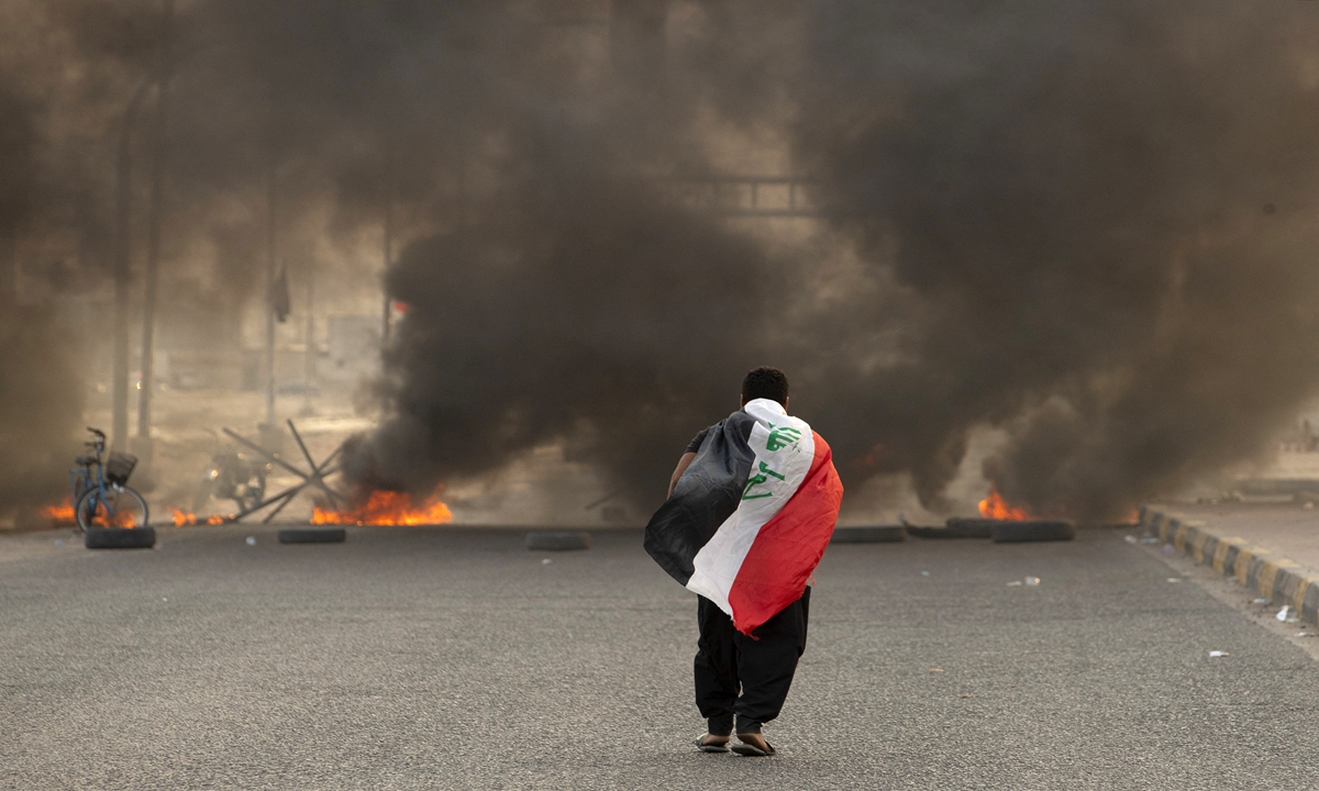 A supporter of Iraqi Shiite cleric Moqtada Sadr carries the Iraqi flag as he walks down a road blocked by burning tires during a demonstration in Iraq's southern city of Basra on August 29, 2022. Dozens of angry supporters of the powerful cleric stormed the Republican Palace, a ceremonial building in the fortified Green Zone, a security source said, shortly after Sadr said he was quitting politics. Photo: AFP