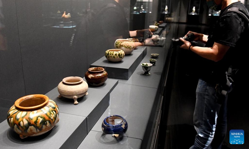 A visitor takes photos of exhibits during a joint exhibition of tri-colored glazed potteries in Zhengzhou, central China's Henan Province, Aug. 30, 2022. The joint exhibition displayed more than 300 tri-colored glazed potteries of the Tang Dynasty (618-907) unearthed from 10 kilns of five provinces in China.(Photo: Xinhua)